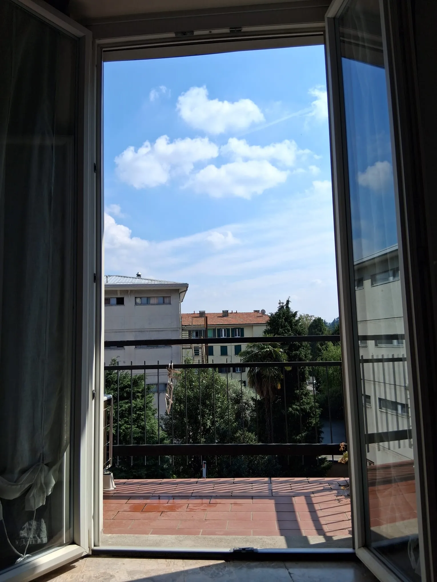 La vue depuis la porte-fenêtre du balcon : arbres, toits et ciel bleu
