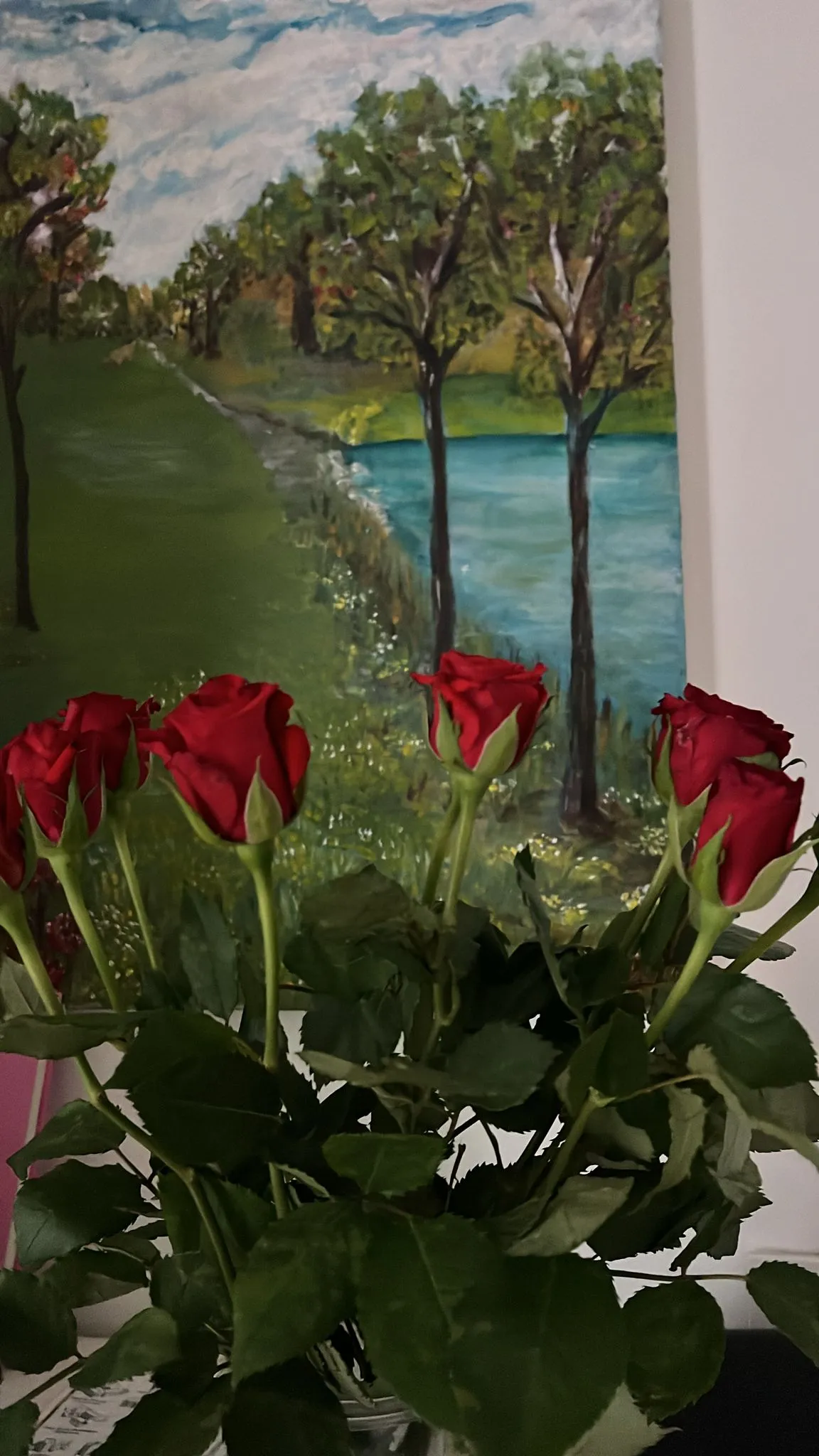 Des roses rouges devant un tableau représentant un lac et des arbres