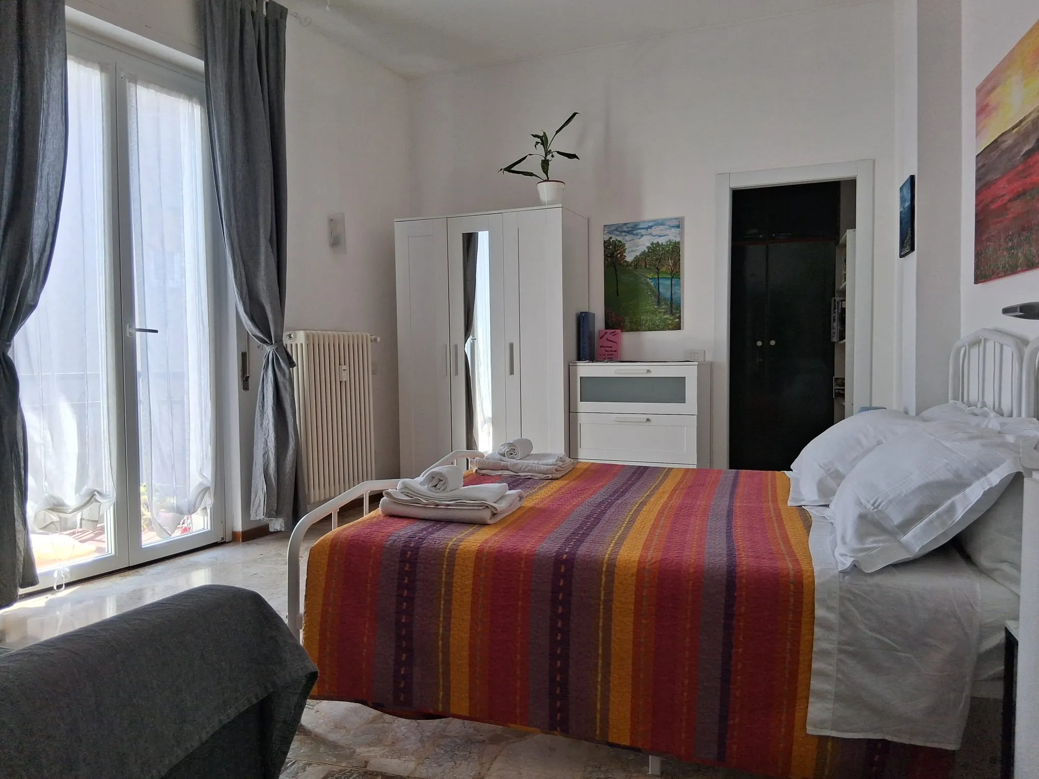 La chambre, avec le lit double, la porte-fenêtre du balcon et une bouteille de prosecco avec deux verres