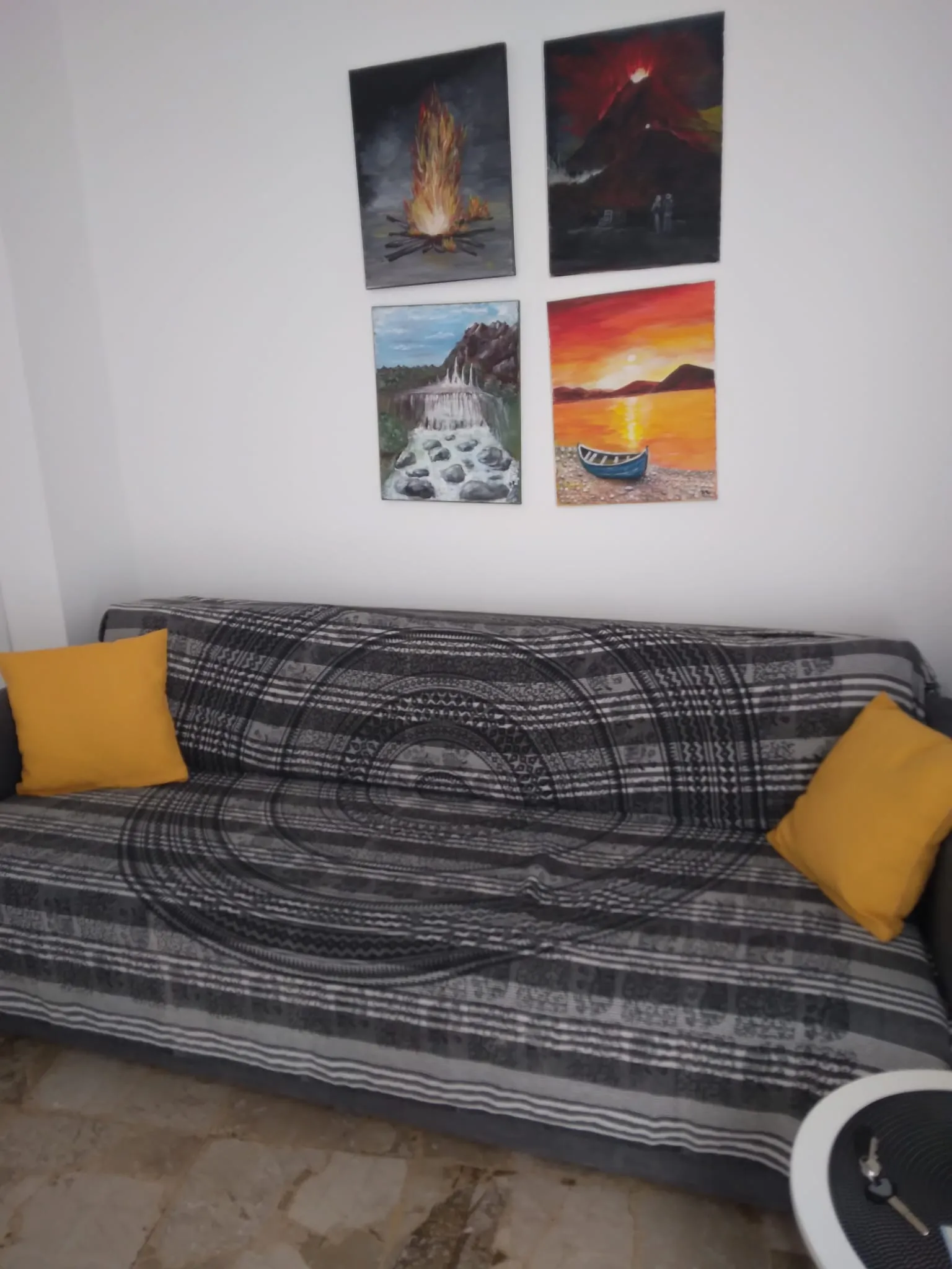 Le canapé, avec des coussins jaunes et quatre petits tableaux